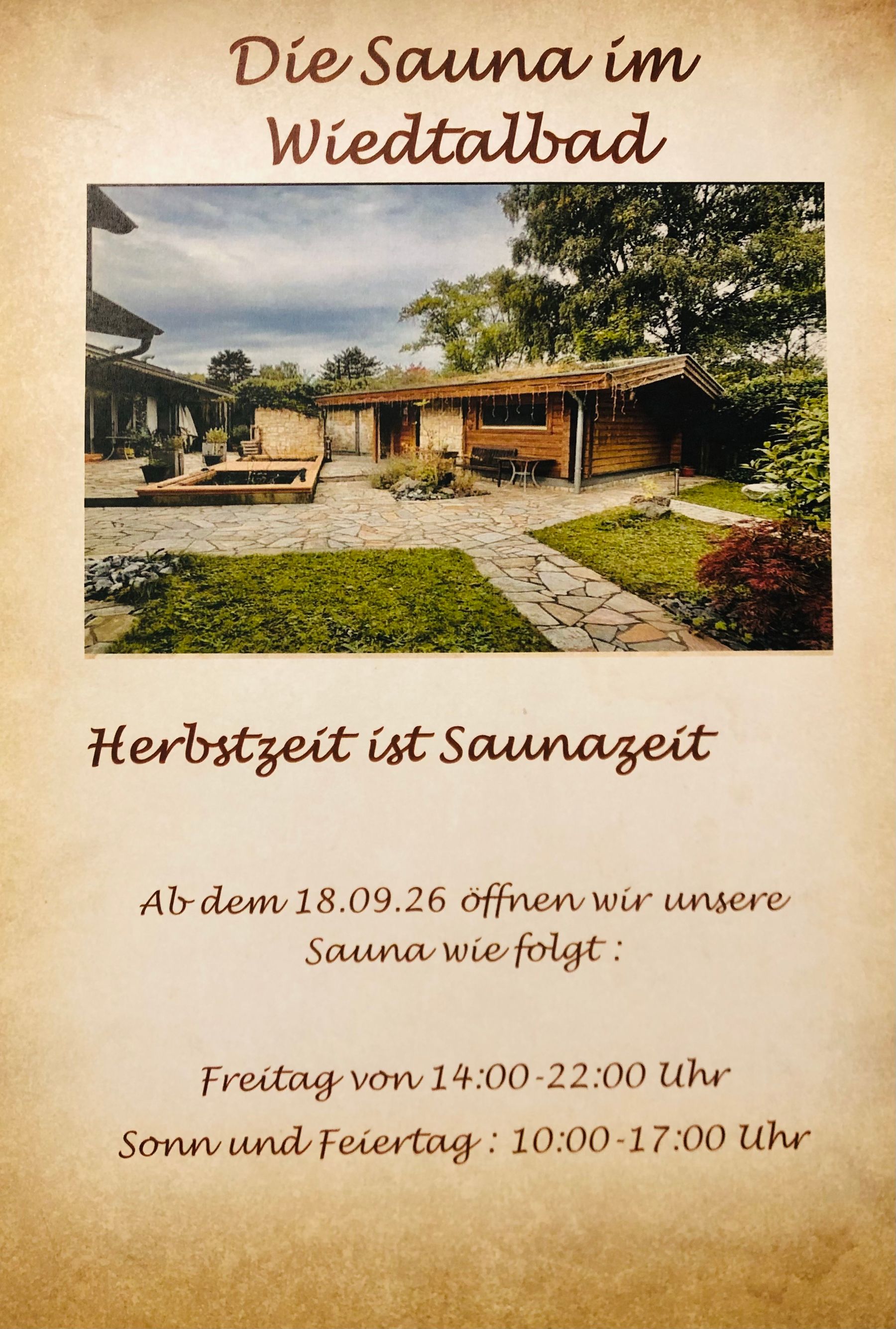 Plakat mit einem Foto eines Saunagebäudes aus Holz und eines Gartens. Der Text gibt die Herbst-Öffnungszeiten der Sauna im Wiedtalbad bekannt: freitags 14:00–22:00 Uhr, sonntags und an Feiertagen 10:00–17:00 Uhr, ab dem 18.09.26.